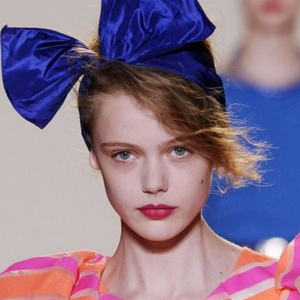 Fashion model Frida Gustavsson walking runway for the Marc Jacobs' show Spring/Summer 2010. She wears an aquamarine bow toping her head and orange - pink striped robe.